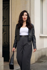 a lady in a white top, a black leather jacket and a pair of grey pants